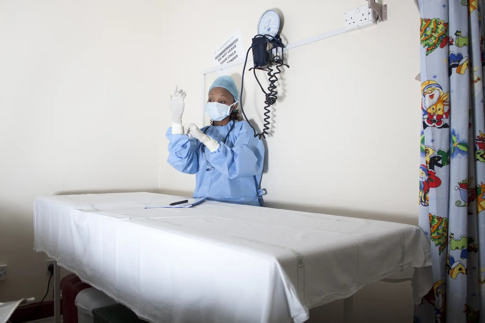 Kenyan nurse in surgical scrubs and mask putting on gloves in a clinic room
